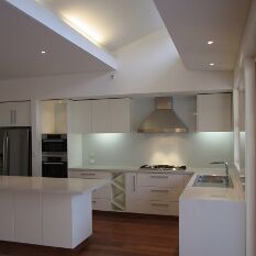 an all-white kitchen with stone benchtops featuring great natural and built-in lighting